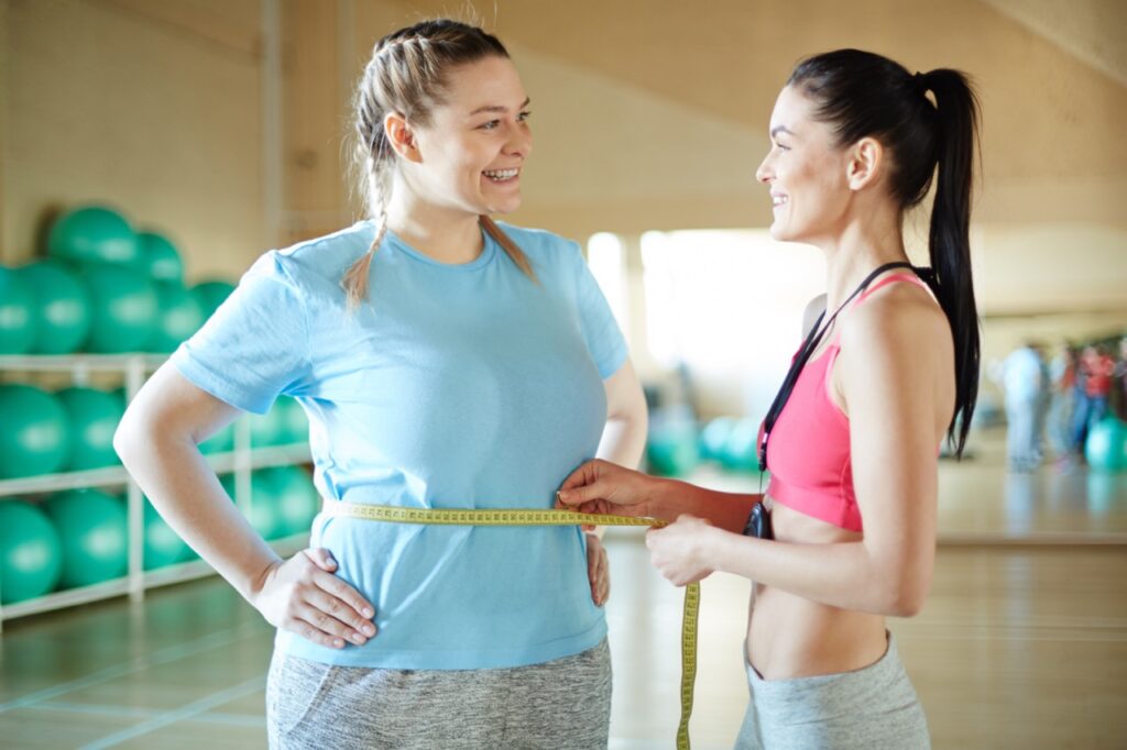 Happy fitness coach measuring waist of overweight woman to check if she's managing a healthy weight.