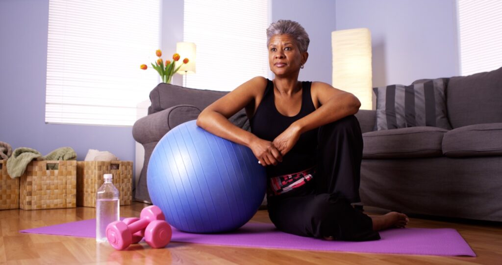 Senior African woman sitting on floor with exercise equipment.