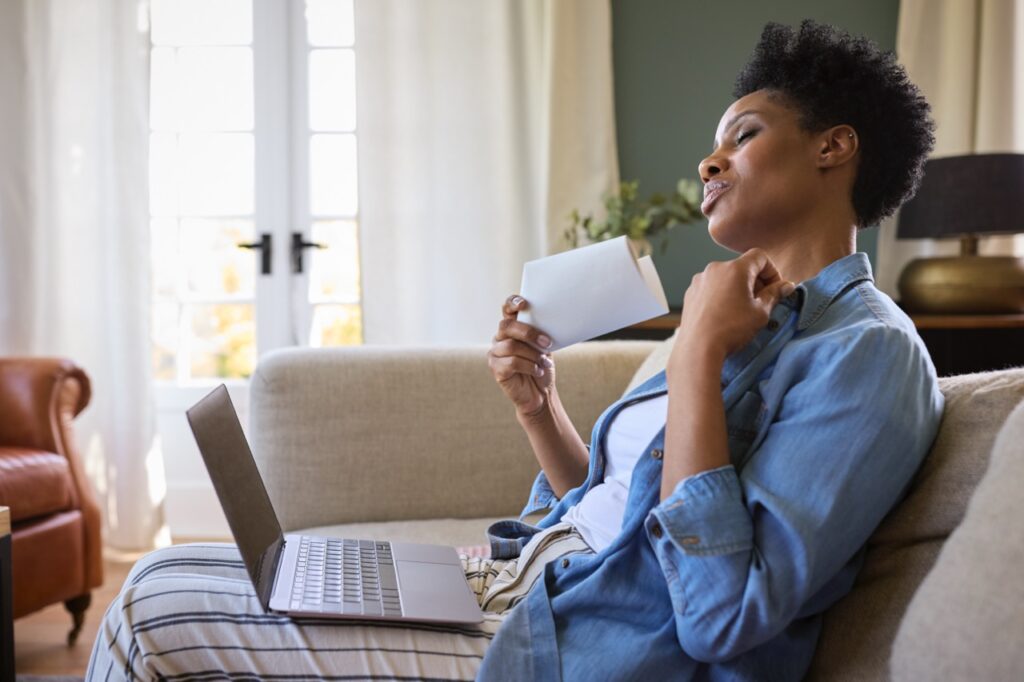 Menopausal mature woman at home with laptop having hot flash fanning herself.