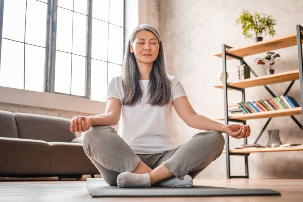 Grey-haired mature Caucasian woman meditating at home.