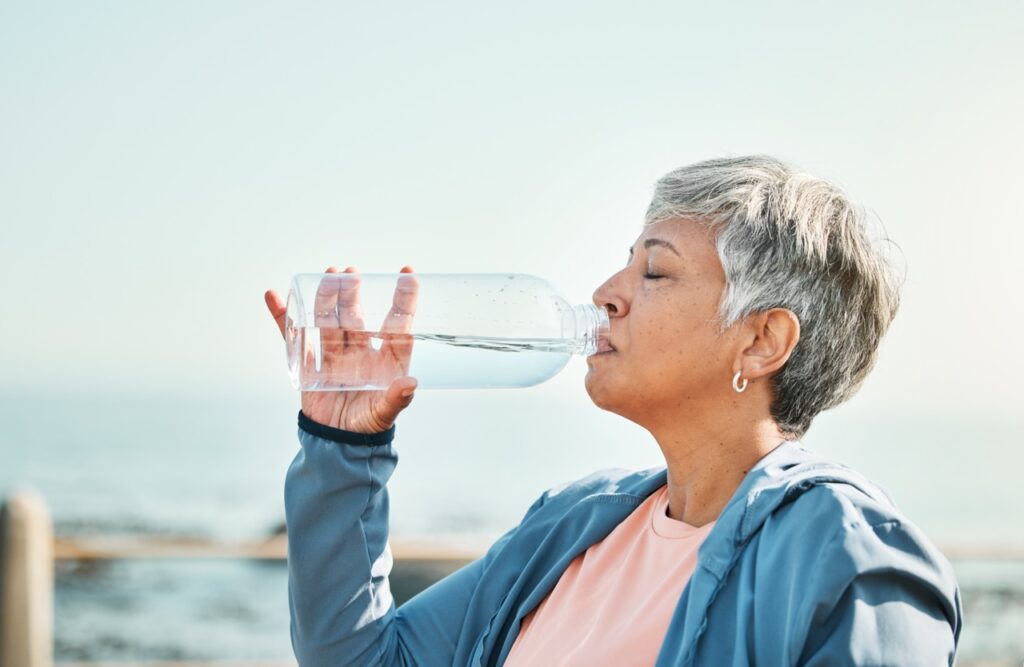 Senior woman, drinking water at the beach.
