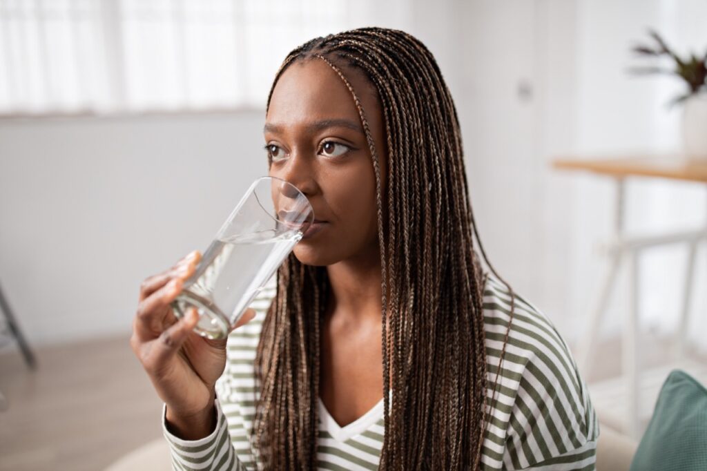 Photo of young black woman drinking fresh water at home.