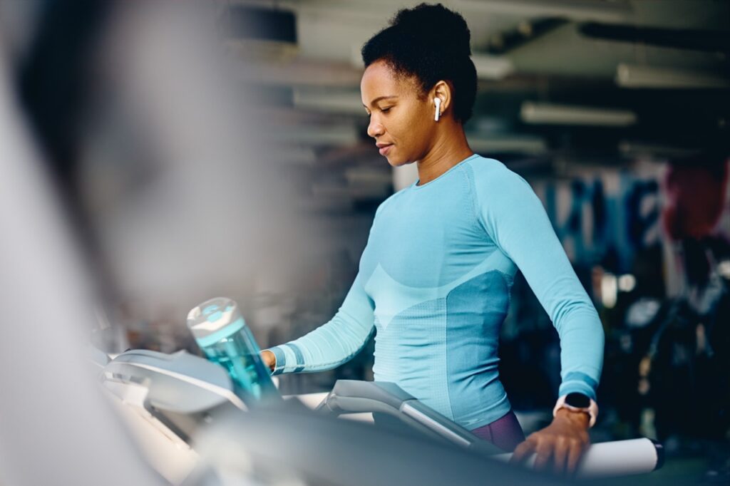 African American athletic woman warming up on treadmill while exercising in health club.