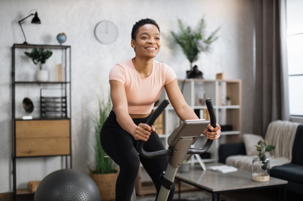 African american woman cycling bike at home in living room.