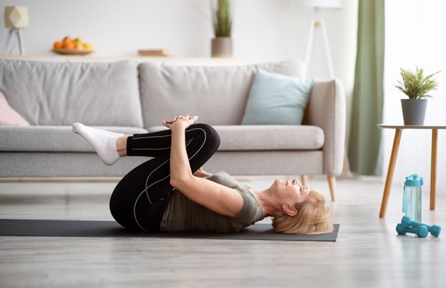 Sporty senior woman doing exercises on yoga mat indoors.