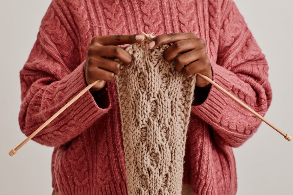 Close up of young African-American woman knitting scarf and wearing cozy sweater.