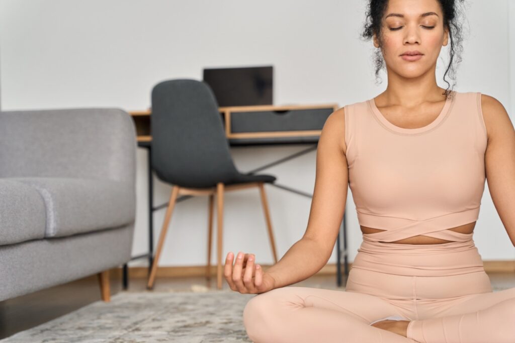 Young healthy African American girl sitting at home in deep meditation.