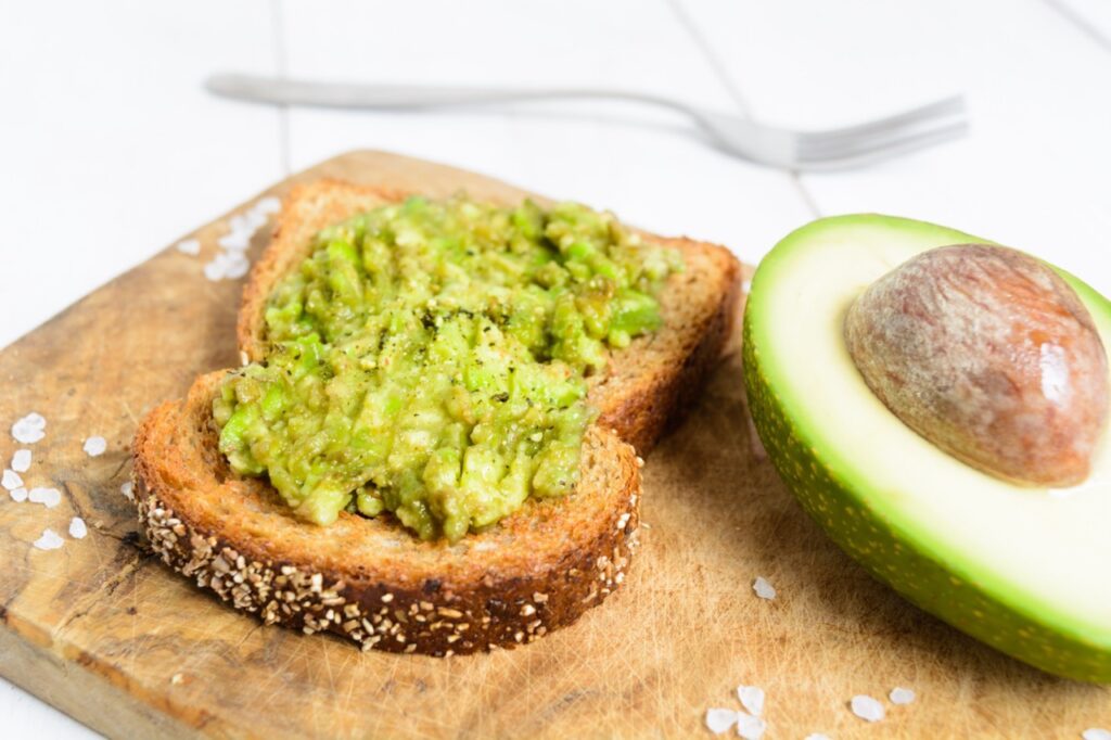 Healthy avocado toast on wholegrain bread on board over white wooden background.