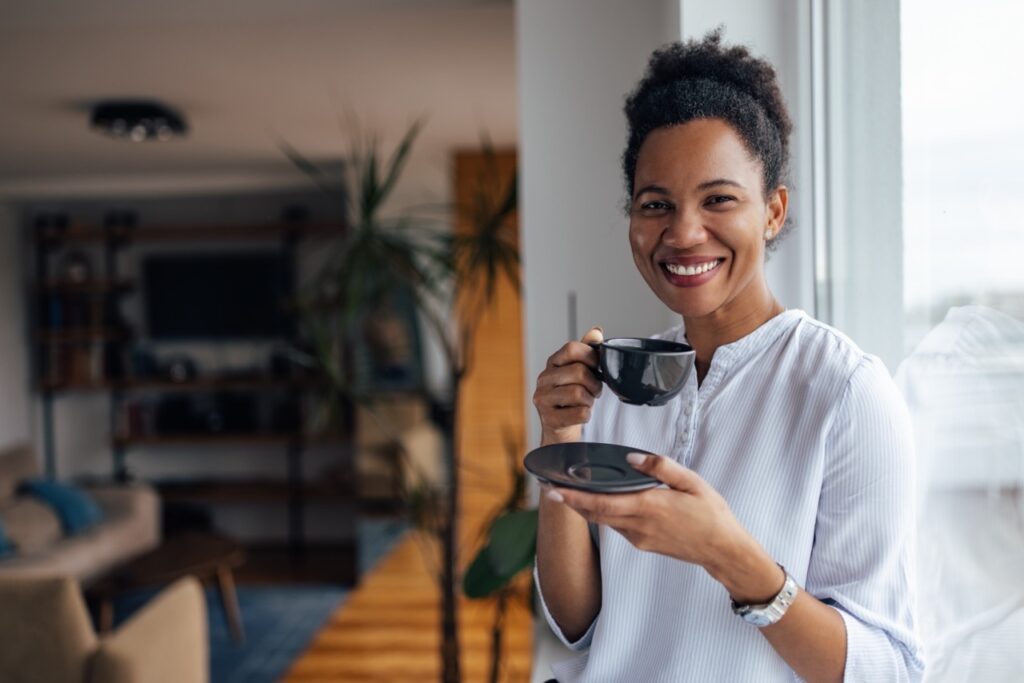 Portrait of happy African woman, looking at camera, while drinking tea.