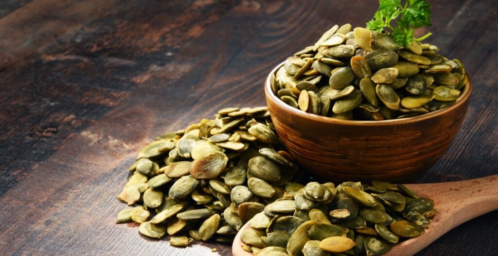 Composition with bowl of pumpkin seeds on wooden table.