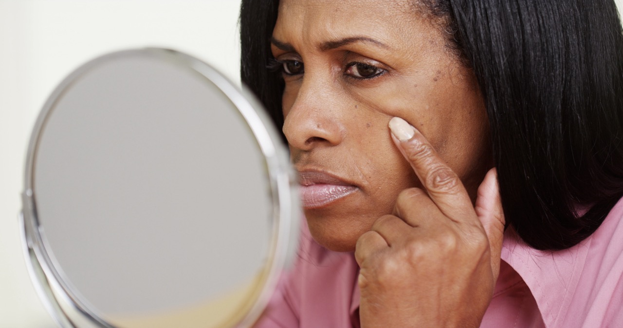 Middle-aged woman examining fine lines and skin texture in a mirror, illustrating menopause-related skin changes