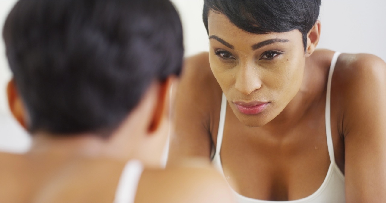 Woman examining dry, uneven facial skin in a mirror, reflecting common skin changes during menopause