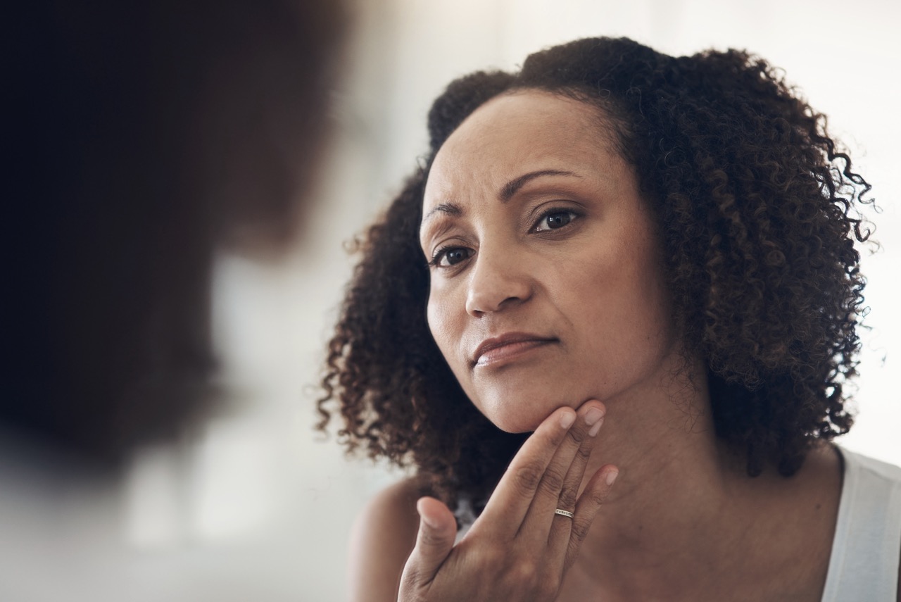 Woman examining her facial skin in a mirror, reflecting common skin changes experienced during menopause